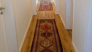 Un pasillo con suelo de madera y un tapete estampado, que conduce a una habitación con radiador.