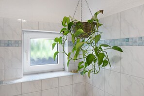 Ein Badezimmer mit Fenster, weißen Fliesen und einer hängenden Pflanze.