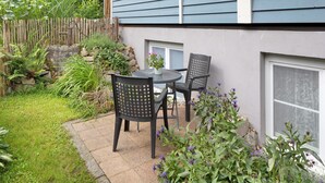 Eine Terrasse mit Tisch und Stühlen, umgeben von einem Garten mit verschiedenen Pflanzen und Blumen.