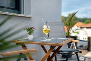 Una mesa con una copa de vino blanco, una planta en maceta y un banco.