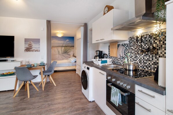 A compact kitchen with a washing machine, a stove, and a dining area with chairs.