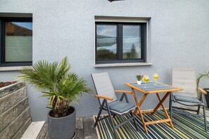 Een terras met een tafel en stoelen, een bloempot en een raam.