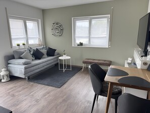 Ett modernt vardagsrum med en grå soffa, ett runt sidobord, en bänk och en matplats med ett träbord och stolar.