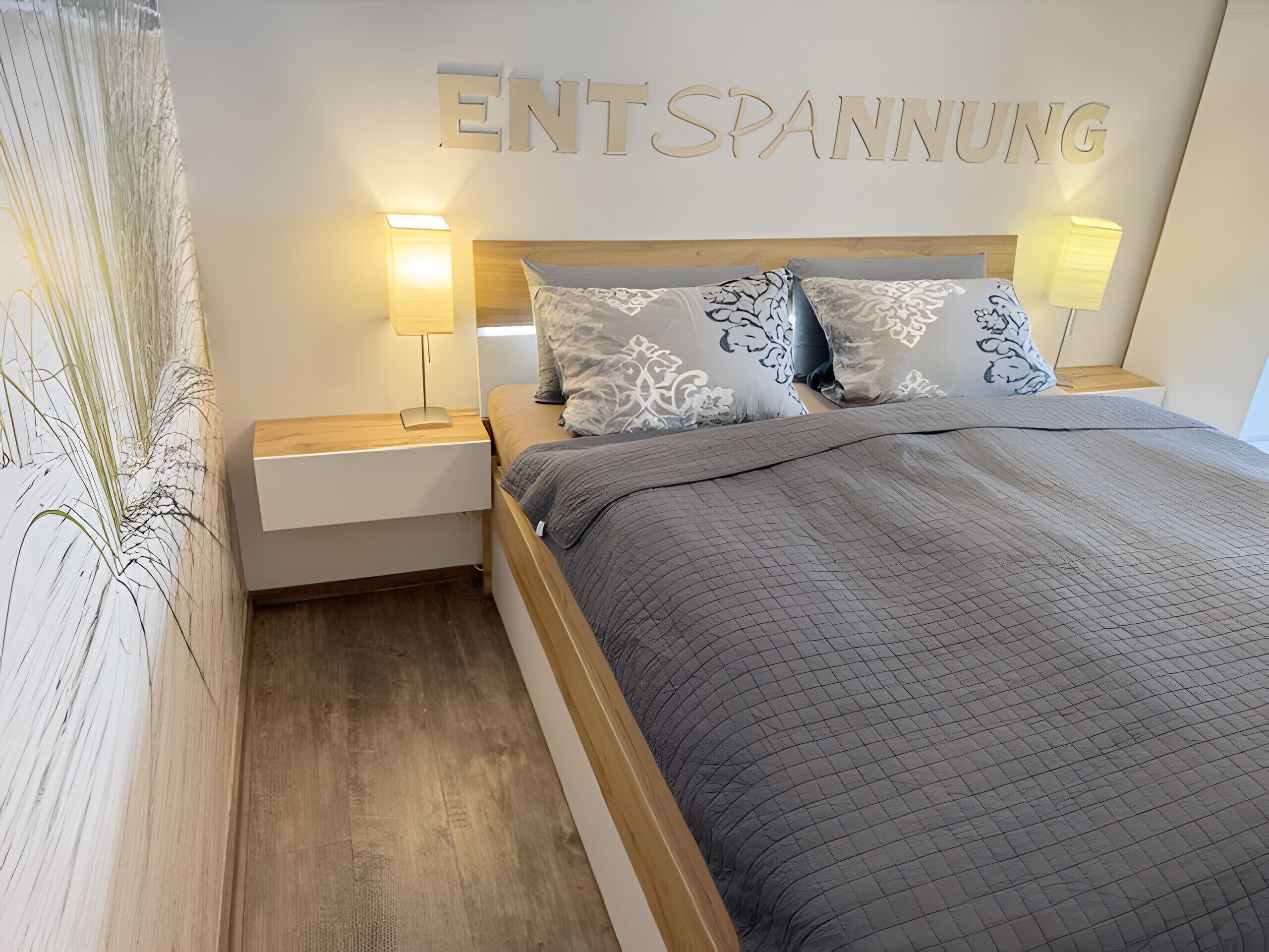 Une chambre d’hôtel avec un lit, deux lampes de chevet, une table de nuit et un mur sur lequel est inscrit en grandes lettres le mot « ENTSPANNUNG ».