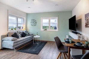A modern living room with a sofa, a dining table with chairs, a TV, and a small side table with a plant.