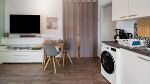 Eine moderne Küche mit Waschmaschine, einer Essecke mit Stühlen, einem Flachbildfernseher und einem Tisch mit Obstschale.