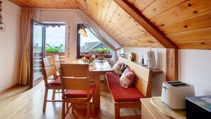 A cozy room with a wooden ceiling, a dining table with chairs, a bench with cushions, a toaster, and a view through a glass door. - Apartment 'Haus Dorfschmiede' with Mountain View, Shared Garden and Wi-Fi (Weilheim)
