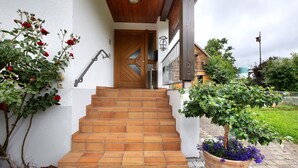 A staircase leading to a wooden door, a potted plant with purple flowers, and a metal railing. - Apartment 'Haus Dorfschmiede' with Mountain View, Shared Garden and Wi-Fi (Weilheim)