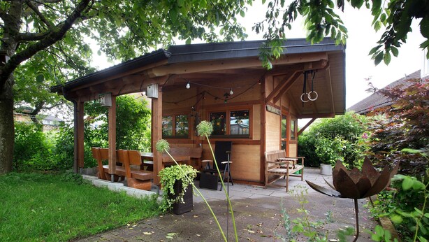 A wooden gazebo with benches, a table, and hanging lights. - Apartment 'Haus Dorfschmiede' with Mountain View, Shared Garden and Wi-Fi (Weilheim)