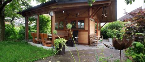 A wooden gazebo with benches, a table, and hanging lights.