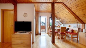 A wooden interior with a TV on a dresser, a dining area with chairs and a table, and a kitchen area with a stove. - Apartment 'Haus Dorfschmiede' with Mountain View, Shared Garden and Wi-Fi (Weilheim)