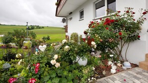A house with a garden full of flowers and plants, a satellite dish, and a view of a green field. - Apartment 'Haus Dorfschmiede' with Mountain View, Shared Garden and Wi-Fi (Weilheim)