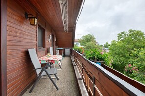 Un balcone in legno con tavolo e sedie, una finestra e vista su del verde.