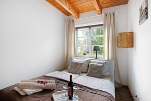 A bedroom with a bed, pillows, a window, and a bottle of wine. - Apartment 'Green Oasis Ferienwohnung' with Shared Terrace, Shared Garden and Wi-Fi (Treia)