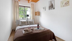 A bedroom with a wooden ceiling, a bed with a brown bedspread, a window with curtains, a bedside lamp, and wall art. - Apartment 'Green Oasis Ferienwohnung' with Shared Terrace, Shared Garden and Wi-Fi (Treia)