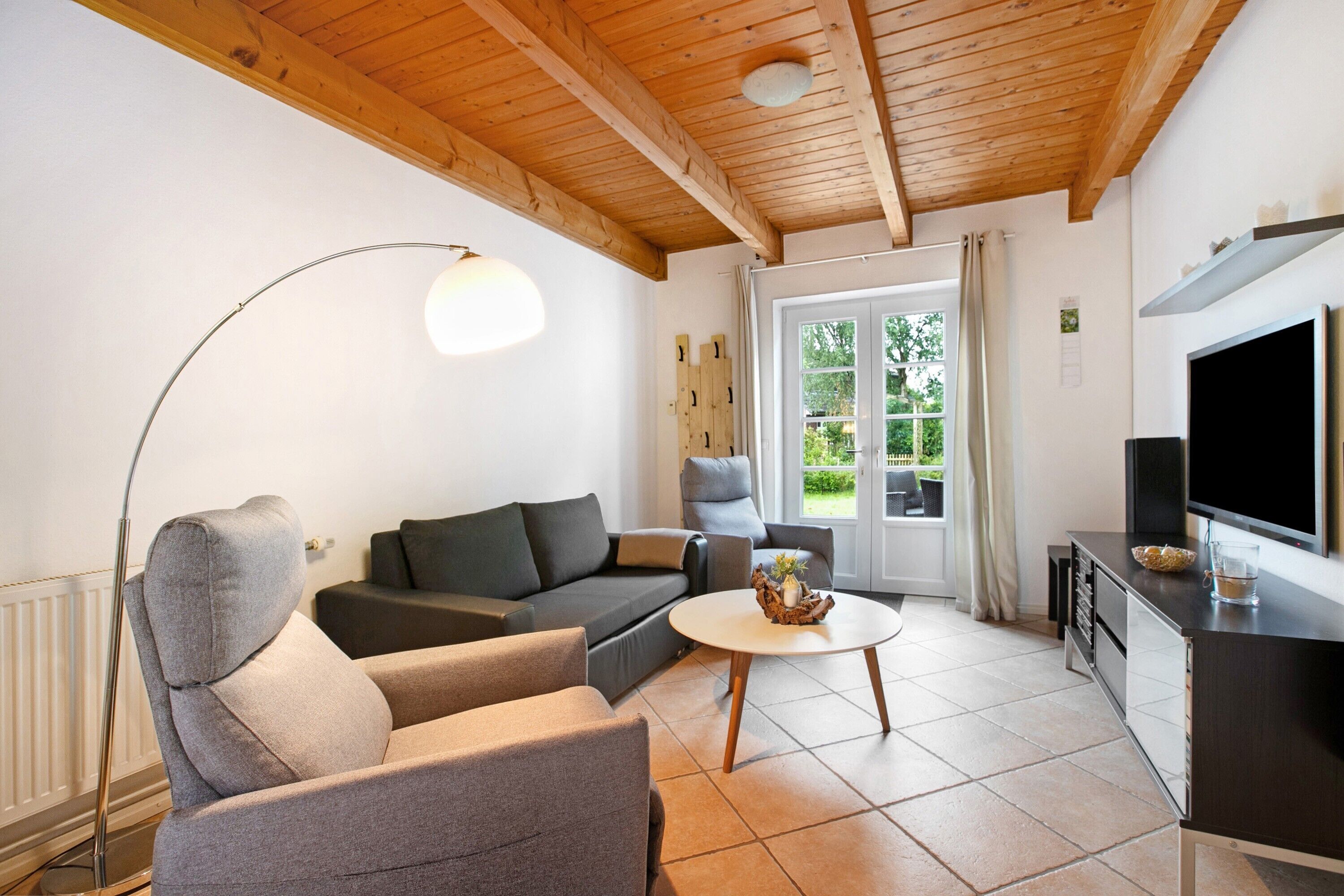 A living room with a sofa, armchairs, a coffee table, a TV, and a window with a view of greenery.