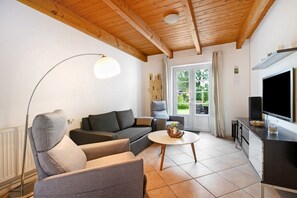 A living room with a sofa, armchairs, a coffee table, a TV, and a window with a view of greenery. - Apartment 'Green Oasis Ferienwohnung' with Shared Terrace, Shared Garden and Wi-Fi (Treia)