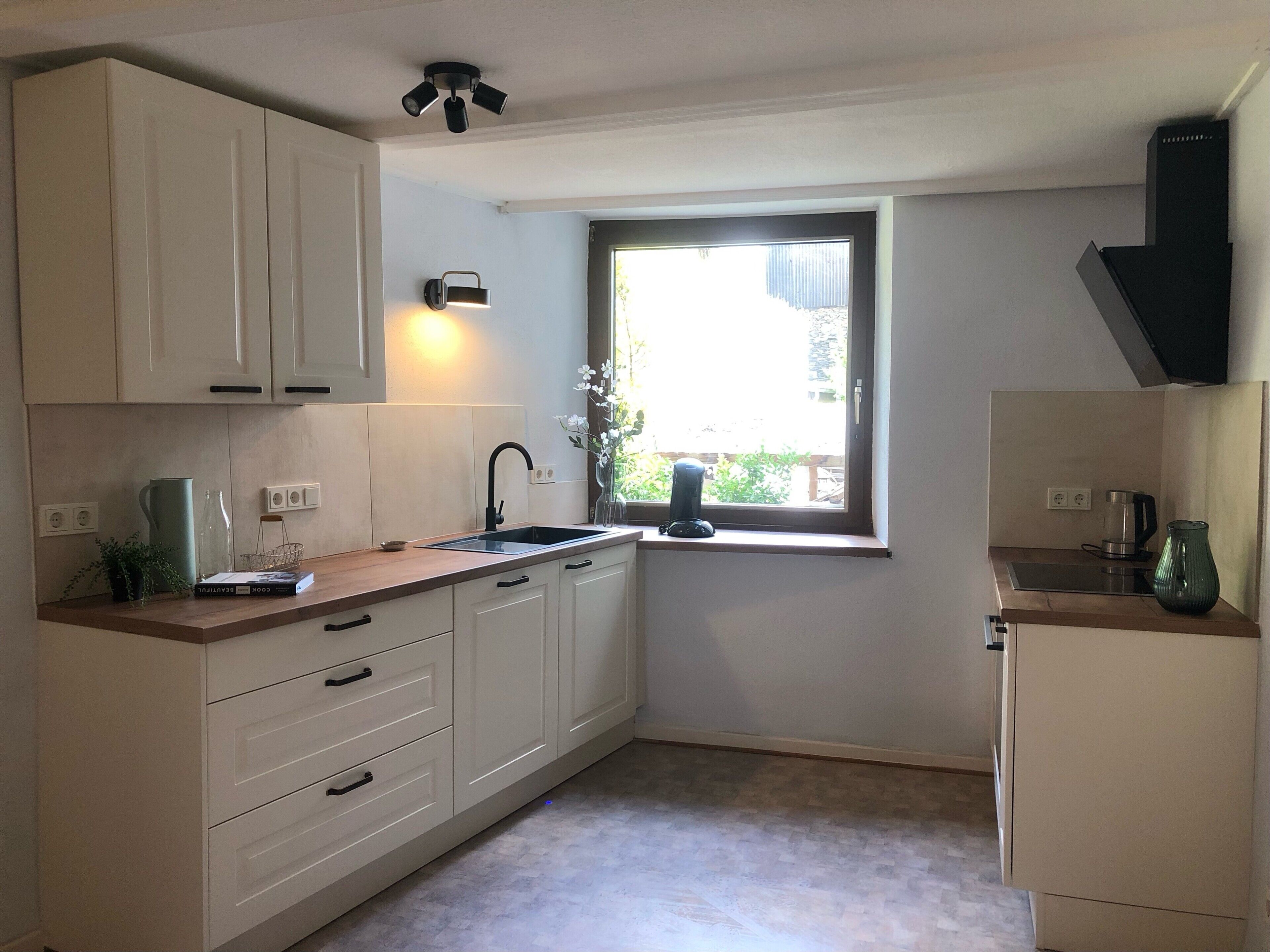 A compact kitchen with white cabinets, a black faucet, a window with a view, and a coffee maker.