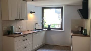 A compact kitchen with white cabinets, a black faucet, a window with a view, and a coffee maker.