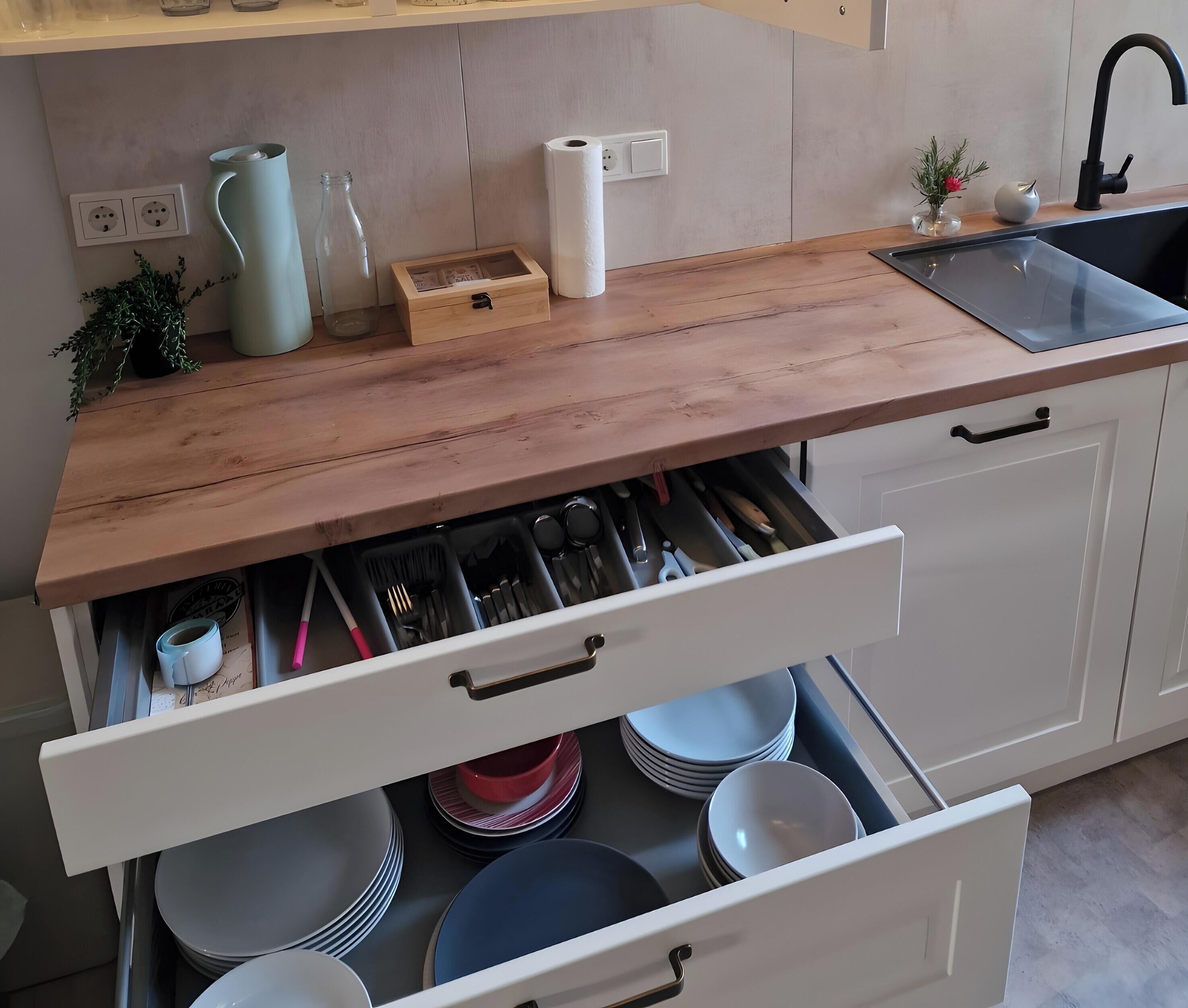 A kitchen with a wooden countertop, a sink, a built-in drawer with utensils, and a small plant.
