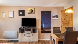 Una sala de estar con televisor de pantalla plana, muebles de madera, una mesa de comedor y un cartel con un cielo nocturno.