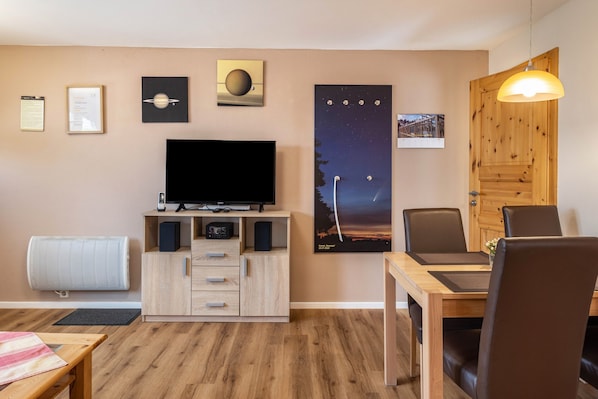 A living room with a flat-screen TV, wooden furniture, a dining table, and a poster of a night sky.