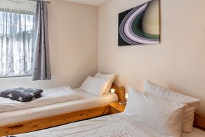 A bedroom with two beds, a window with curtains, a bedside lamp, and a wall-mounted abstract painting.