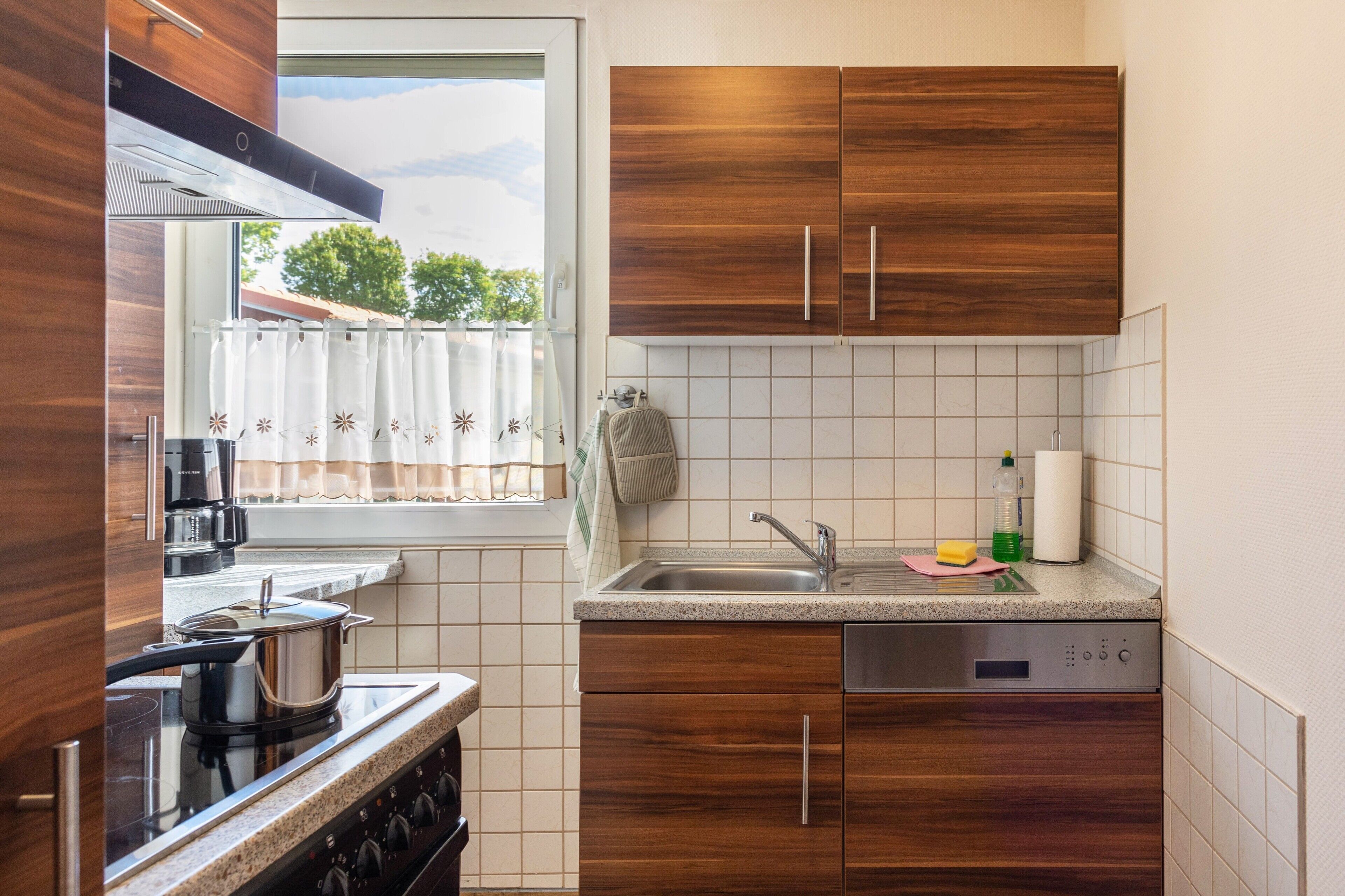 Een keuken met houten kastjes, een roestvrijstalen spoelbak en een vaatwasser.