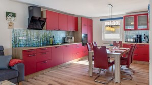 Eine moderne Küche mit roten Schränken, ein Essbereich mit roten Stühlen und ein Holzboden.