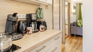 A kitchenette with a coffee maker, kettle, and mug, a wooden countertop, and a sofa in the background. - Holiday Home 'Ferienhaus Biber' with Private Terrace, Private Garden and Wi-Fi (Stechow-Ferchesar)