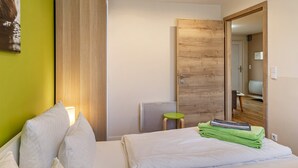 A bedroom with a bed, a green wall, a wooden door, and a small stool. - Holiday Home 'Ferienhaus Biber' with Private Terrace, Private Garden and Wi-Fi (Stechow-Ferchesar)