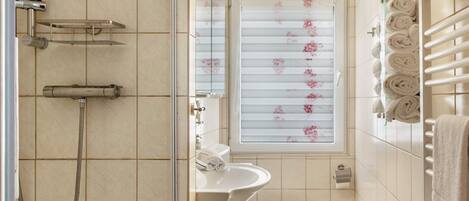 Ein Badezimmer mit Dusche, Toilette, Waschbecken und einem Fenster mit floralem Sichtschutz.