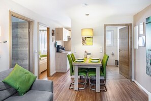 A modern kitchen with a dining table set for four, green chairs, and a pendant light.