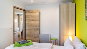 Habitación de hotel con cama, toalla verde, armario de madera, espejo, radiador y pared verde.