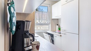 Una cocina compacta con cafetera, una taza, una ventana con vistas y armarios blancos.