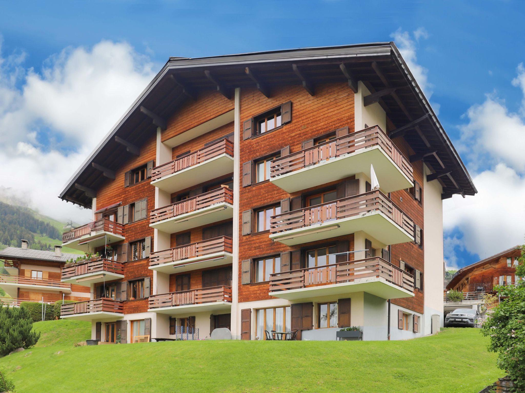 A multi-story hotel with balconies, a flat roof, and a mountainous backdrop.
