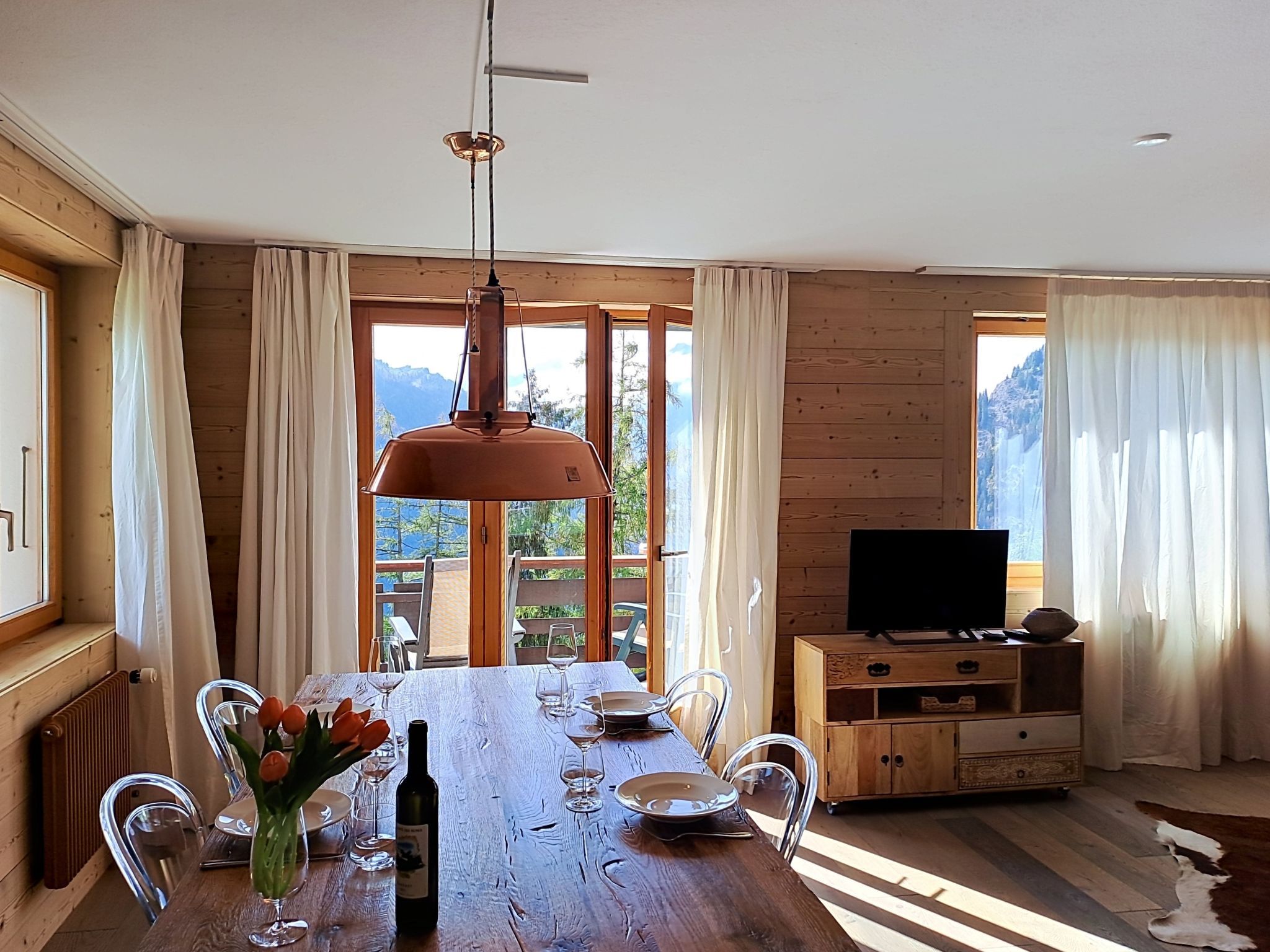 Un'area pranzo con tavolo in legno, sedie, una bottiglia di vino e una televisione su un mobile in legno.