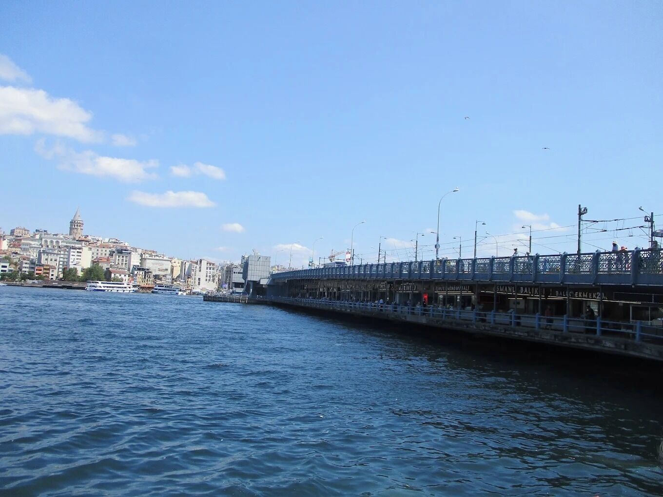 A waterfront promenade with a bridge, buildings, and a boat dock.