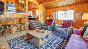 Ein gemütliches Blockhaus-Interieur mit Holzwänden, einem Essbereich und einem Wohnzimmer mit Sofa und Sesseln.
