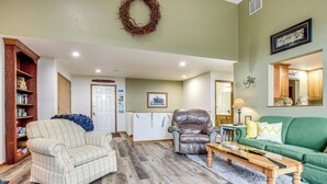 Una sala de estar con una mesa de centro de madera, un sofá verde, un sillón de cuero y un sillón blanco.