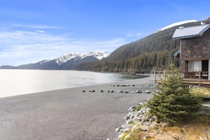 Une cabane dotée d’une terrasse donnant sur un lac, entourée de montagnes et de forêt.