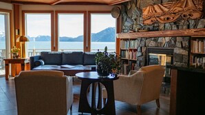 Un salon chaleureux avec une cheminée en pierre, une grande fenêtre donnant sur un lac et une bibliothèque remplie de livres.