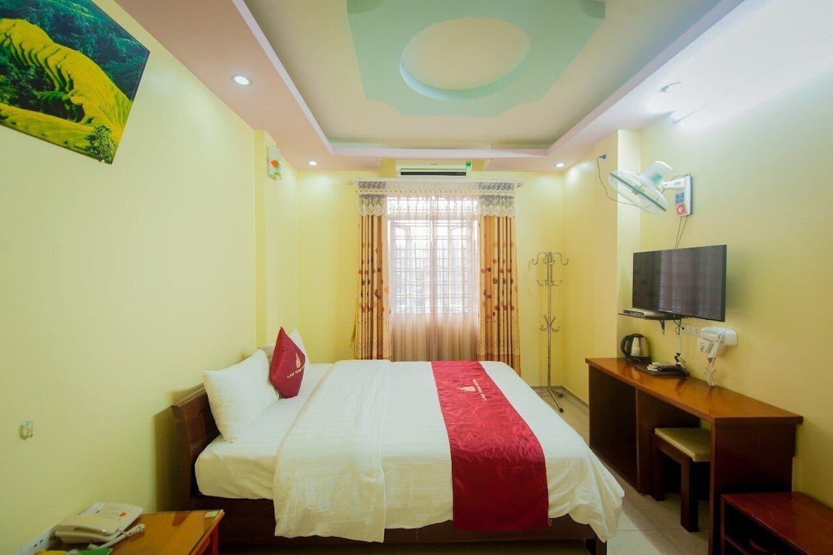 A hotel room with a bed, a desk, a television, and a window with curtains.