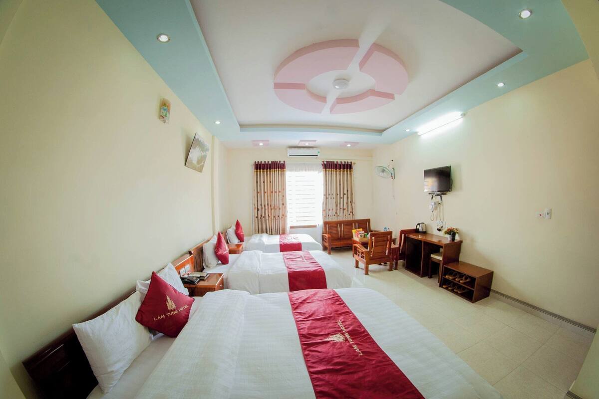 A hotel room with two beds, a desk, a chair, a TV, and a shoe rack.