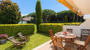 Eine Terrasse mit Tisch und Stühlen, umgeben von ordentlich geschnittenen Hecken und Bäumen.
