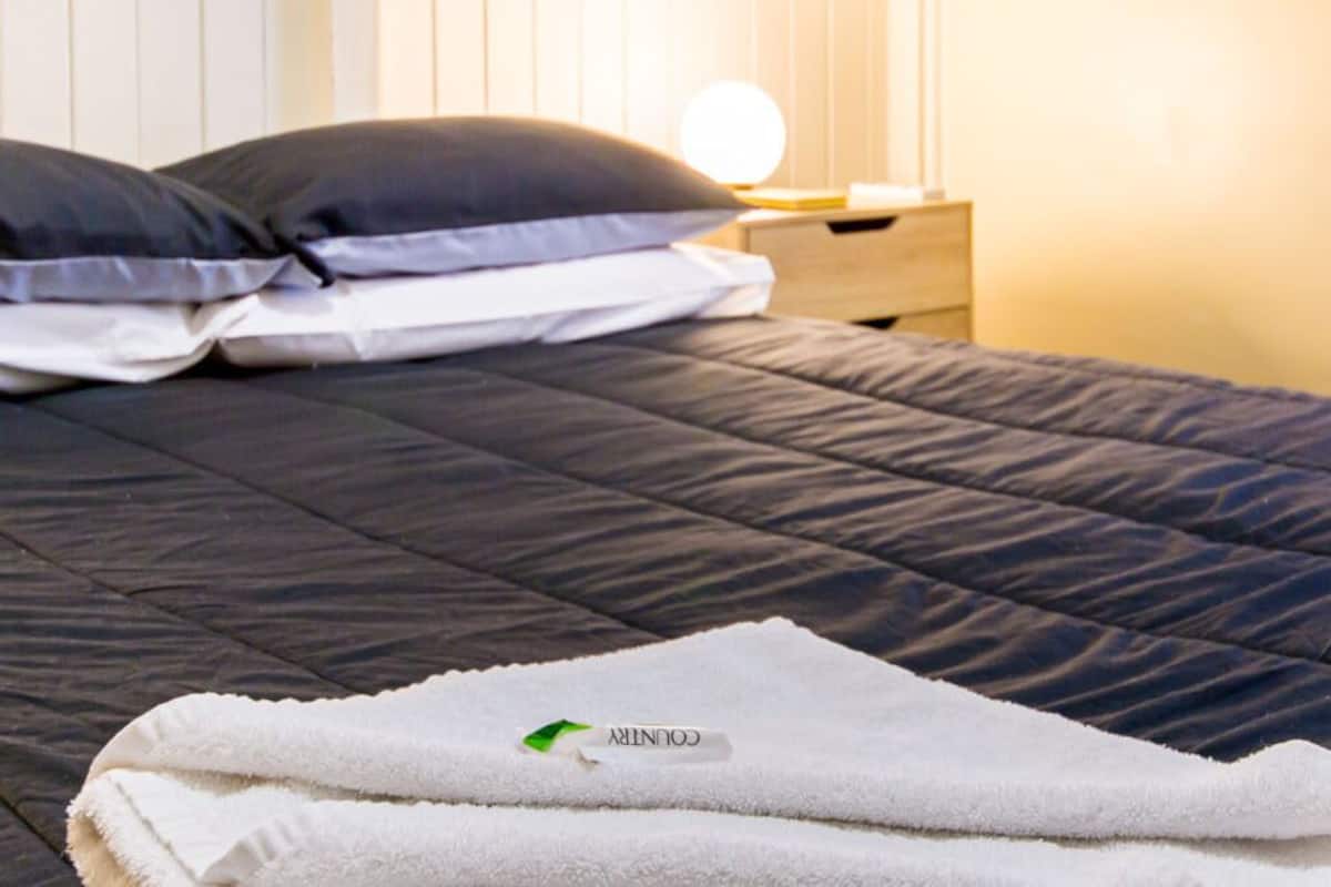A neatly made bed with a dark quilt, two pillows, and a folded white towel on the side.
