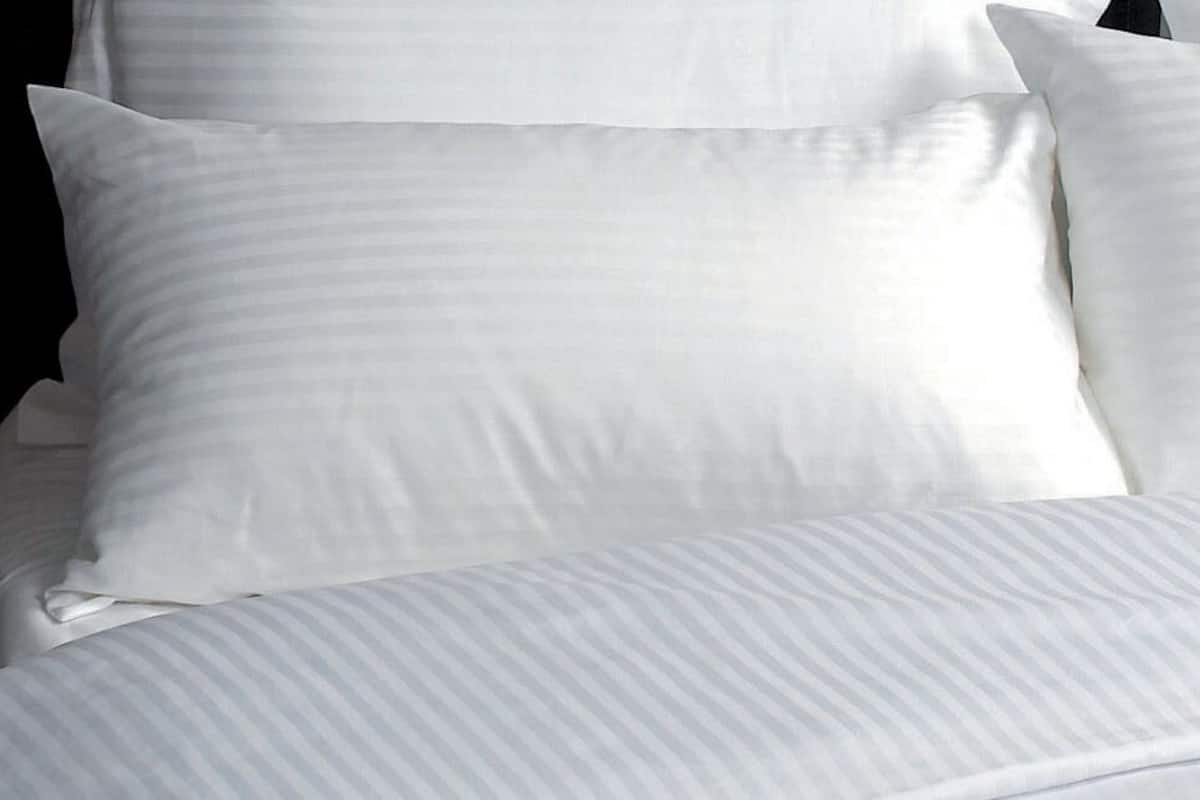 A neatly made bed with white linens and pillows.