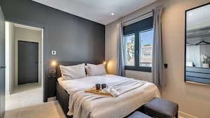 Ein modernes Schlafzimmer mit einem großen Bett, Nachttischen, einer Bank und einem Fenster mit Vorhängen.