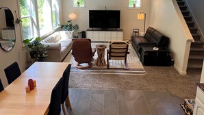 En moderne stue med spiseplads, et fladskærms-tv og en trappe.