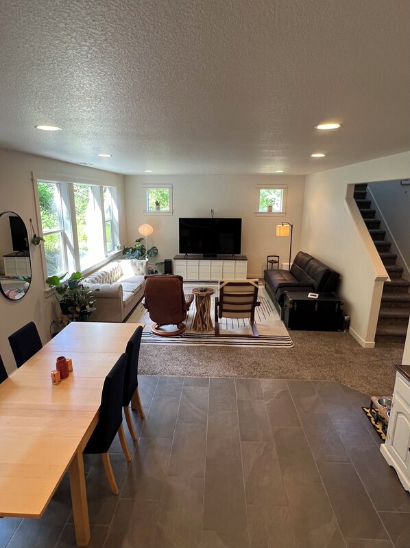 A modern living room with a dining area, a flat-screen TV, and a staircase.